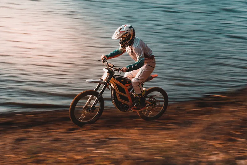 Moto elétrica 79BIKE acelerando na beira de um lago ao pôr do sol